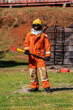 Vertical picture of the firefighter stands outdoors holding an iron axe with confidence.