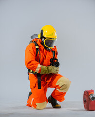 Fototapeta premium Vertical picture of firefighter sitting kneel down while holding and looking to the fire hose on white background.