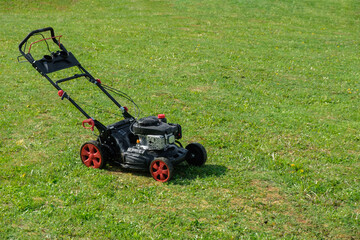 Obraz premium Gasoline lawn mower on the freshly mowed backyard garden plot with copy space. Mowing dandelions. Lawn care, spring work in the garden.