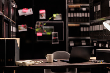 Investigator workplace with laptop and coffee cup on desk. Private detective agency office with evidence board hanging on wall, shelf full of folders and table at night time