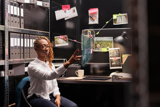Private investigator comparing holographic clues in incident room, investigating evidence and insight. Female detective working with augmented reality and artificial intelligence.