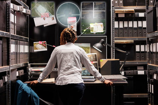 Young detective looking at hologram in incident room, trying to solve felony with evidence and insight. Private investigator examining holographic images with artificial intelligence at desk. - Powered by Adobe
