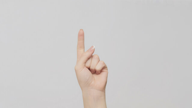 Hand gesture. One number. Woman counting pointing finger up on light gray background.