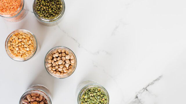 Legumes in glass jars top view on white background. Vegetable protein, healthy eating. Copy space