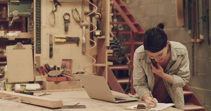 Carpenter woman, laptop and phone call in workshop for small business planning and management. Female person speaking on smartphone and writing carpentry schedule and information for creative project