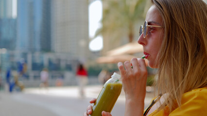 Young woman in dress drinking detox smoothies through a straw from bottle. 