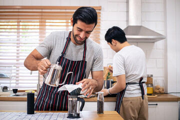 Diversity of LGBT relationships. A gay couple living together concept. Two guys of different ethnicity having warm conversation while making coffee on kitchen at home.