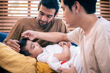 Diversity of couple man touching forehead of sick little boy son at home, caring parent father...