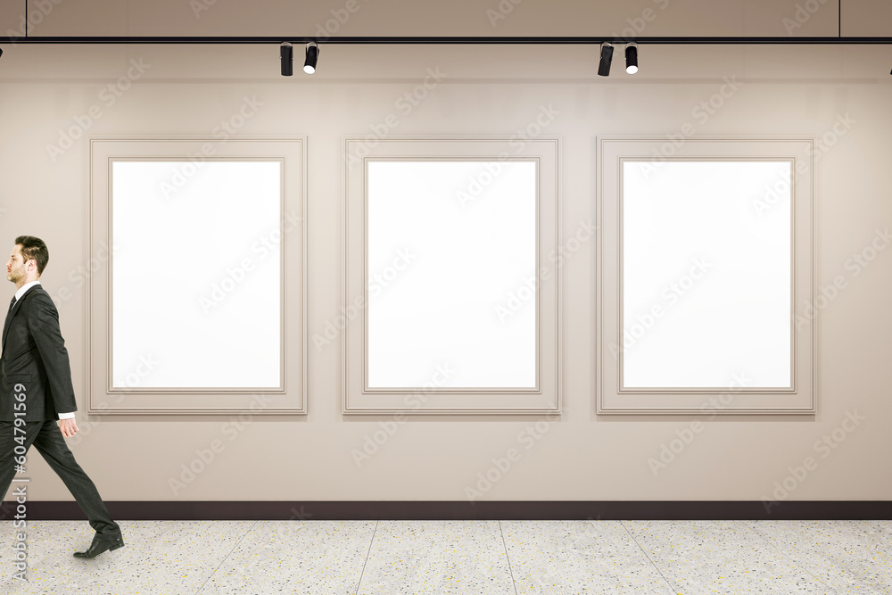 Poster man walking past three blank white image frames on the wall in modern abstract gallery interior, moc