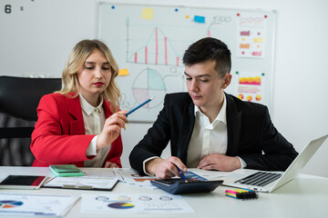 Two financial analysts working together with paper charts and laptops at office