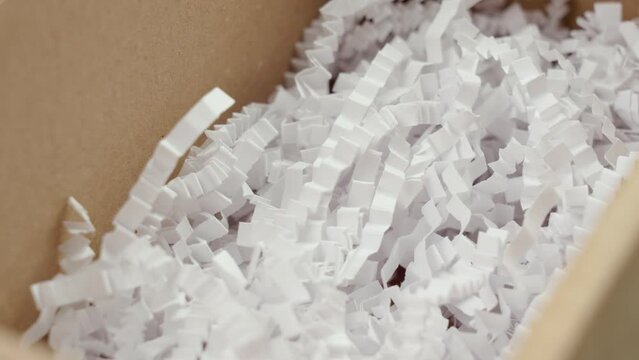Open cardboard box with white shredded plastic filler close up. Rotation