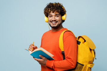 Young teen Indian boy student wear casual clothes backpack bag headphones listen music write down...