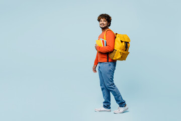 Full body side view young teen Indian boy student he wearing casual clothes backpack bag hold books walk go isolated on plain pastel light blue cyan background. High school university college concept. © ViDi Studio