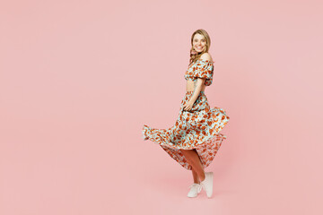 Full body side profile view fun happy nice young blonde caucasian woman wear summer casual clothes waving long skirt isolated on plain pastel light pink background studio portrait. Lifestyle concept.