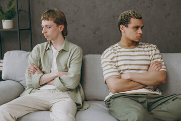 Young sad mad grumpy couple two gay men wear casual clothes together ignore each other sit on sofa couch at home flat rest spend free spare time in living room Pride day june month love lgbtq concept - obrazy, fototapety, plakaty