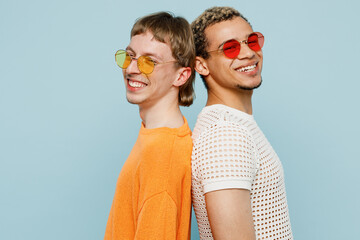 Fototapeta Side view young happy couple two gay men wearing casual clothes sunglasses together stand back to back isolated on plain blue color background studio portrait. Pride day june month love LGBTQ concept. obraz