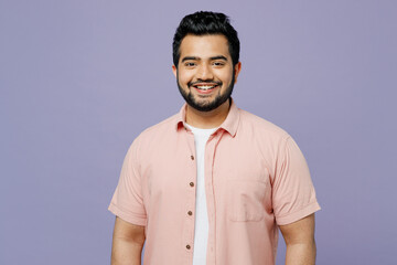 Young smiling happy fun joyful cool Indian man wearing pink shirt white t-shirt casual clothes looking camera isolated on plain pastel light purple color background studio portrait. Lifestyle concept.