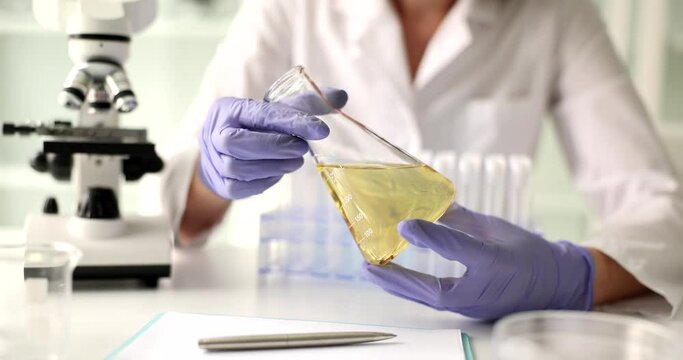 Scientist hand in protective gloves holds yellow liquid in flask closeup. Analysis of oil and oil products