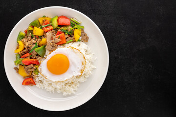 streamed rice topped with stir fried beef with black pepper, red, yellow, green sweet pepper, bell pepper or capsicum, spring onion and egg in ceramic plate on dark tone texture background, top view