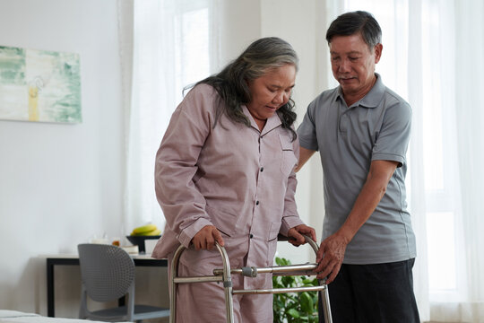 Husband helping sick wife to move around the house leaning on walker