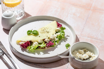 French vegetarian omelet filled with feta cheese and green salad for breakfast on pink tile background with clear shadows in hard light, menu