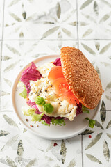 Breakfast burger with scrambled eggs, green salad and tomatoes slices on printed tile background with text space, copy space