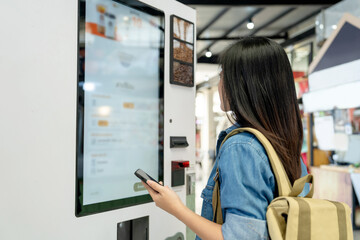 Asian woman ordering drink from touch screen electronic machine in shopping mall, electronic menu.