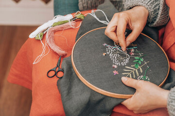 Hands of fashion designer doing embroidery on fabric with thread at workshop