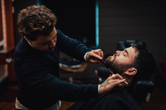 Barber cutting beard of customer in shop
