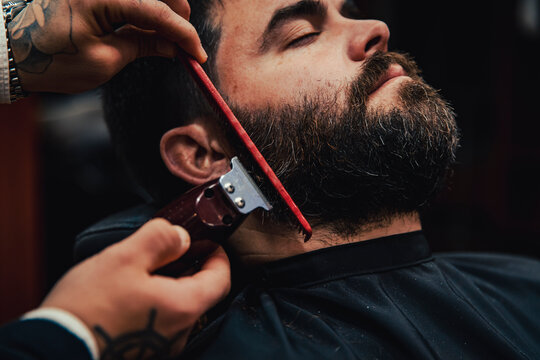 Customer with eyes closed getting beard trimmed in barber shop
