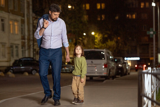 Father holding son's hand waking on sidewalk in city at night