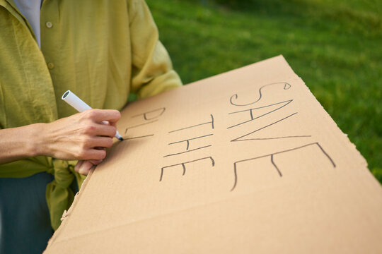 Woman writing Save The Planet text with felt tip pen on cardboard cut out in garden