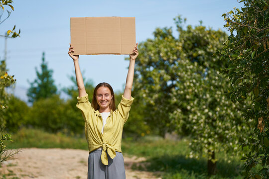 Smiling Woman Holding Cardboard Cut Out With Arms Raised In Garden