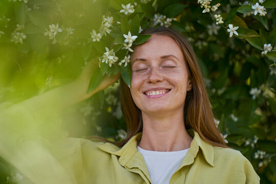 Smiling woman with eyes closed by orange blossom flower in garden