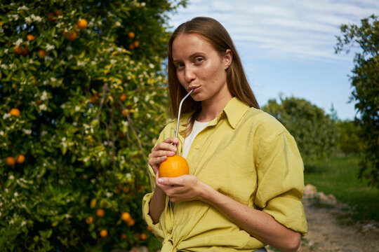 Woman drinking orange juice through reusable metal straw in orchard