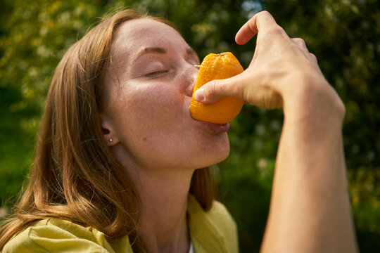 Woman with eyes closed eating fresh orange at orchard