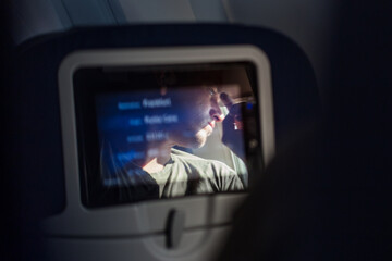 Reflection of a passenger on an airplane touch screen monitor during long flight. Entertainment service system in aircraft