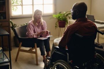 Psychologist discussing with patient sitting on wheelchair at office