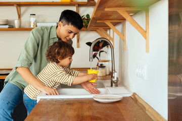 Son filling water in glass through faucet by mother in kitchen at home