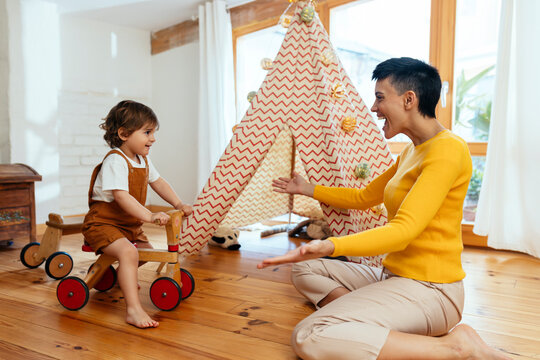 Cheerful woman playing with son sitting on cycle at home