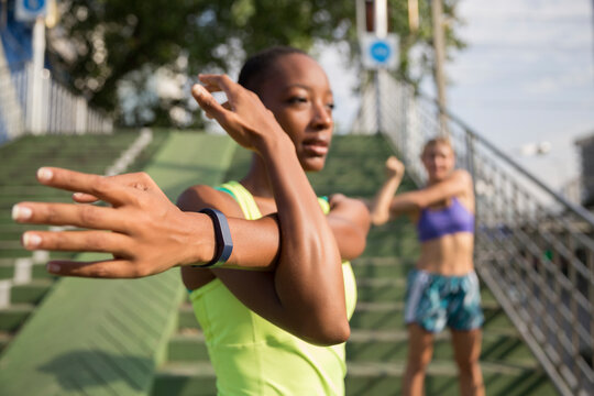 Woman wearing fitness tracker stretching with friend