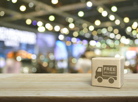 Free delivery truck icon on wood block cube on wooden table over blur light and shadow of shopping mall, Business transportation service concept