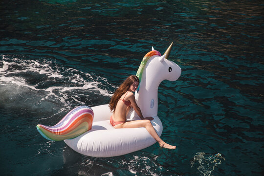 Girl sitting on unicorn air mattress in sea at vacation