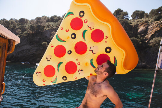Shirtless man holding pizza shaped air mattress at vacation