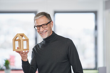 Portrait of smiling senior architect holding model house in office