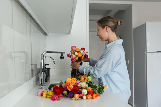 Woman Arranging Ranunculus In Vase On Kitchen Counter At Home