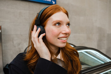 Young woman listening music with headphones and smiling while standing on escalator