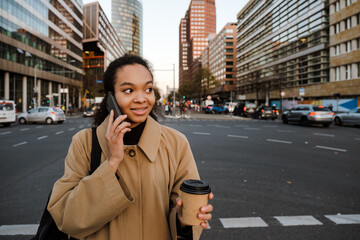 African girl talking on mobile phone and drinking coffee while walking outdoors