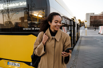 Obraz premium Smiling afro girl using smartphone while standing outdoors