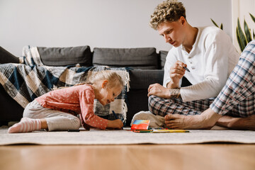 Father and his daughter drawing while sitting on floor in living room